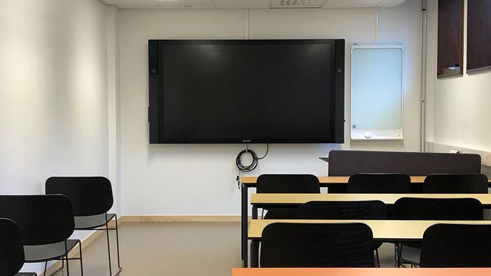 Et lite undervisningsrom med pulter, stoler, skjerm og en liten tavle