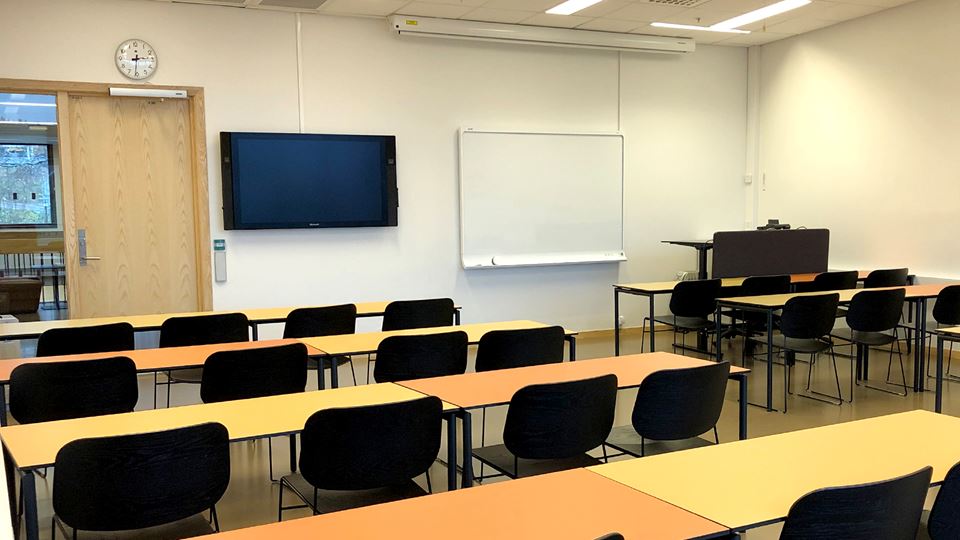 Undervisningsrom med pulter og stoler på rekke. Tavle og skjerm fremme.
