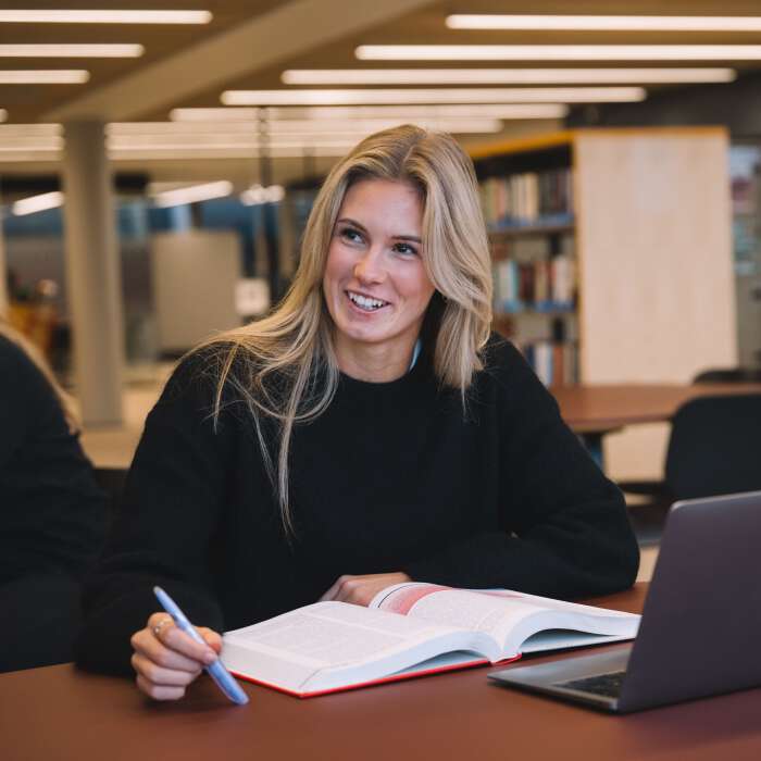 A student studies at the library with an open book and PC.