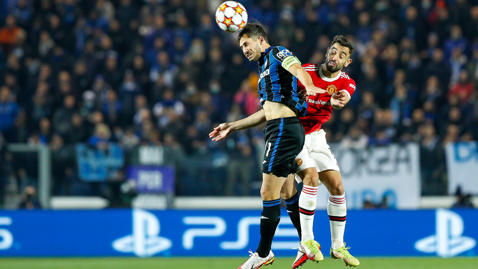 Two footballers jumping to head the ball, football stands in the background