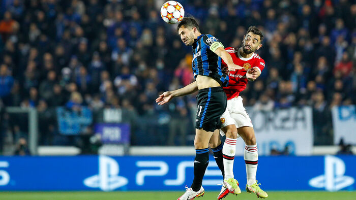 Two footballers jumping to head the ball, football stands in the background