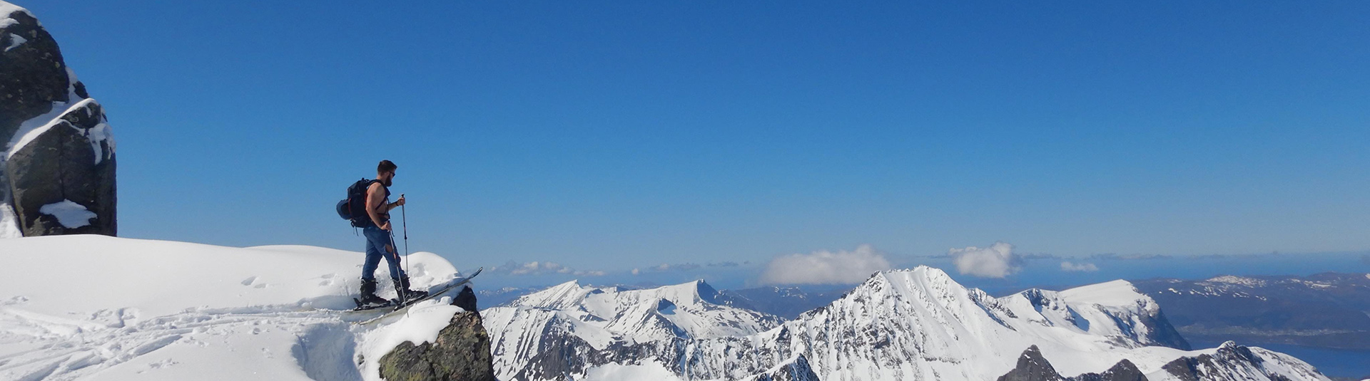 A young man on skis look out over a snowy, sunny mountain landscape