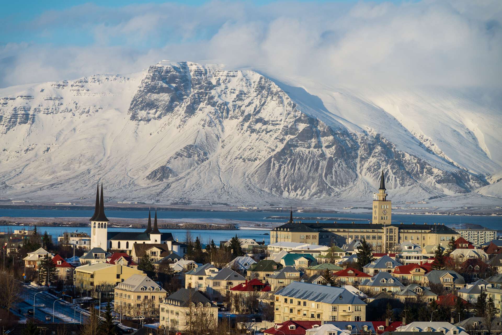 Utsikt over Reykjavík med Hallgrímskirkja i forgrunnen og snødekte fjell i bakgrunnen.