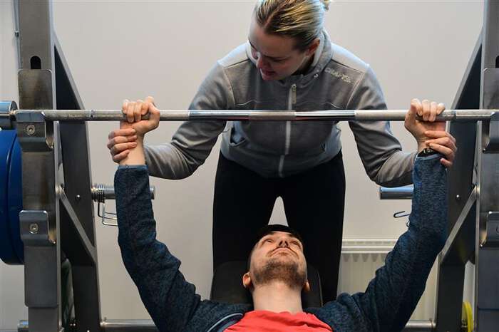 En deltager får hjelp av en trener med å utgjøre benkpress