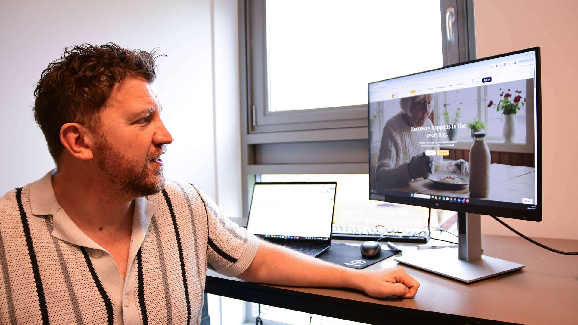 Mann sitter på kontoret og viser frem en pc-skjerm. 