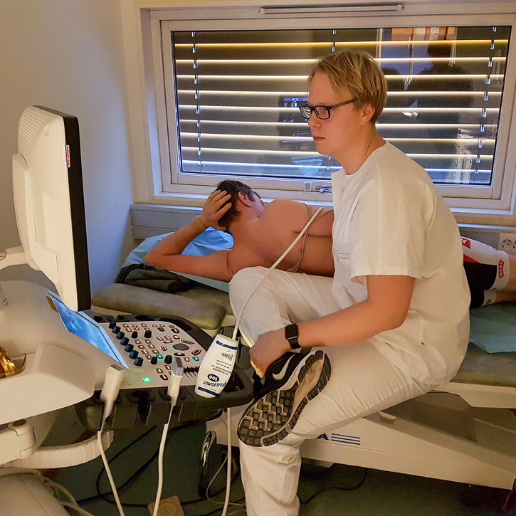 A young nurse holding an ultrasound device against a participant’s back as he lies prone