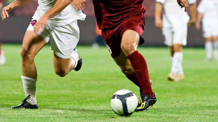 To football players compete for control of the ball on the pitch