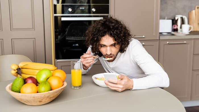 Mann som et frukost og scrollar på mobilen. 