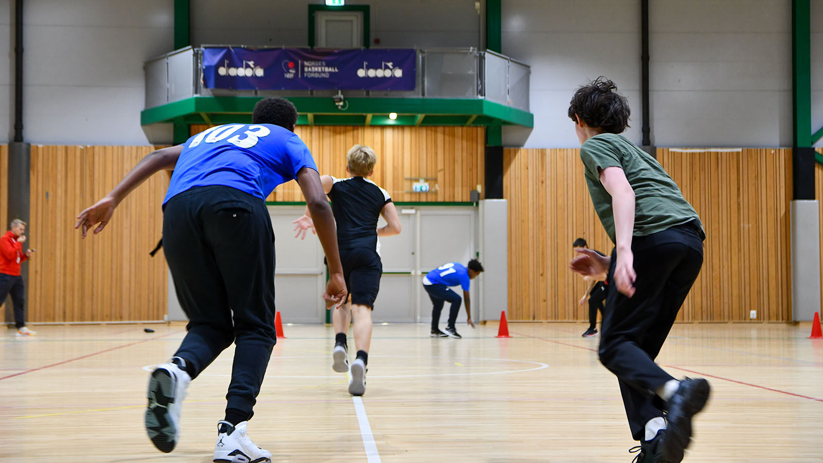 Bildet viser en gruppe ungdommer som løper i en gymsal mot en vegg