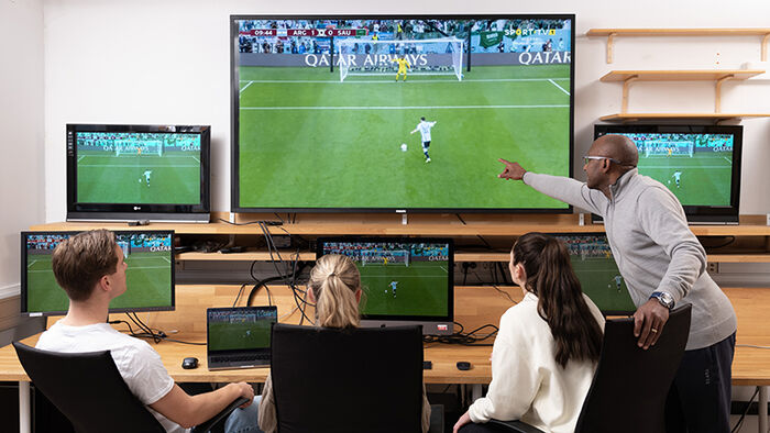 Teaching in the ball laboratory, surrounded by screens with footage of a football game