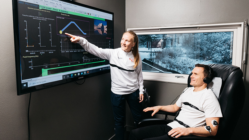 Researcher points to results on screen to a participant who sits in a chair