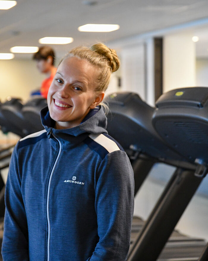 Sara smiles in front of treadmills at the gym 