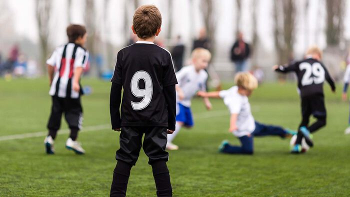 Gutter som spiller fotball. En av dem står og ser på.
