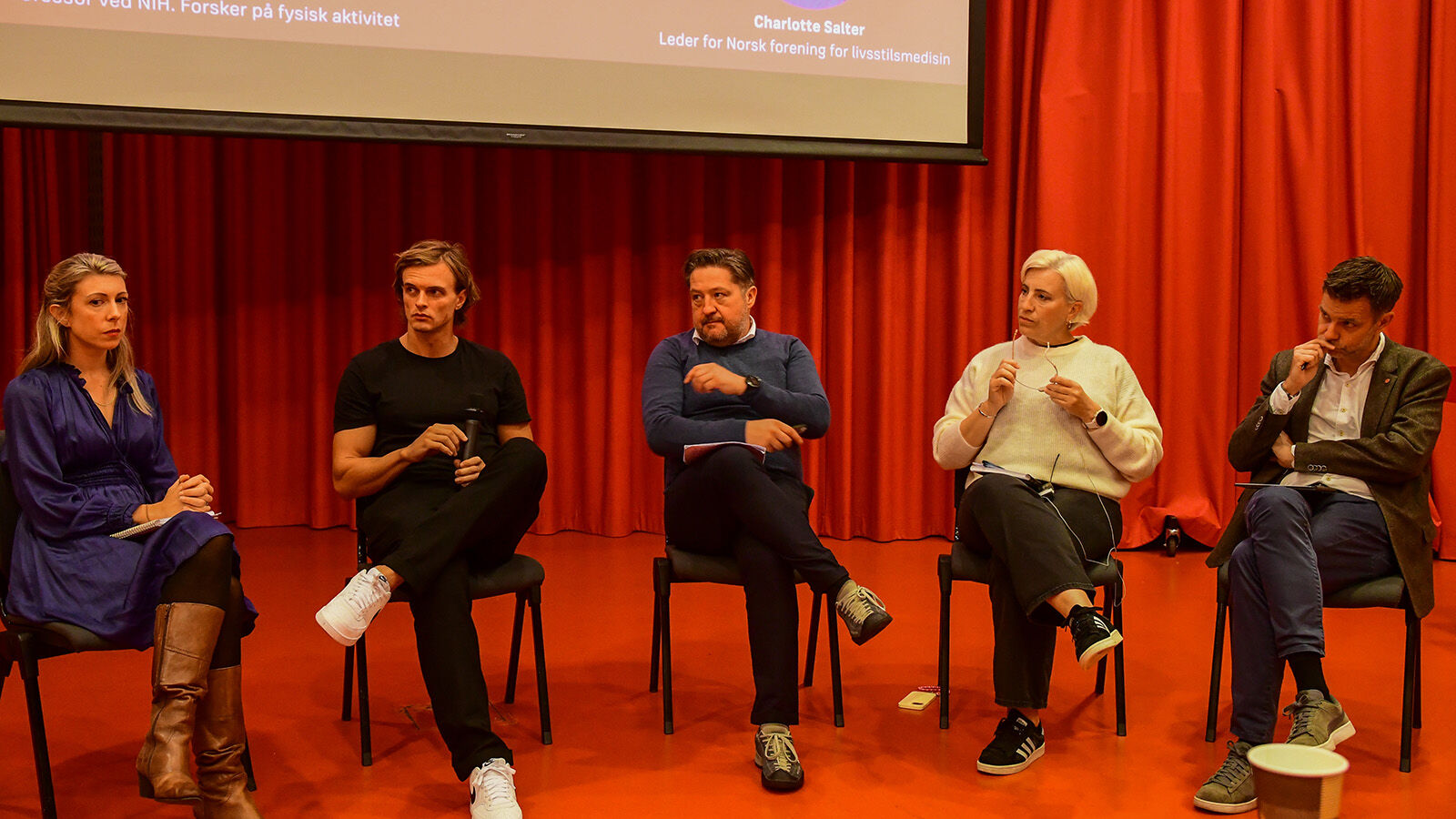 Fem paneldeltakarar på scenen i auditorium.