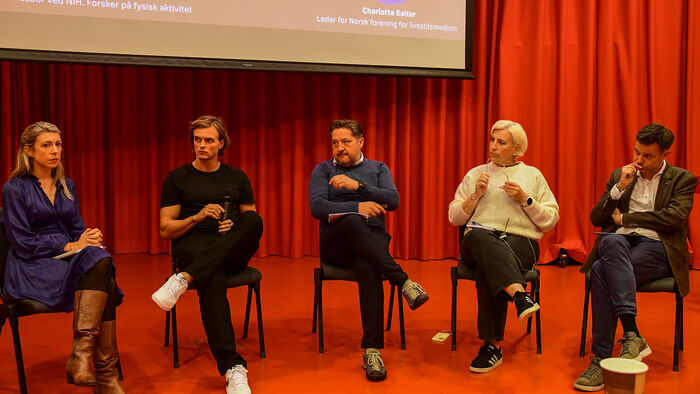 Fem paneldeltakarar på scenen i auditorium.
