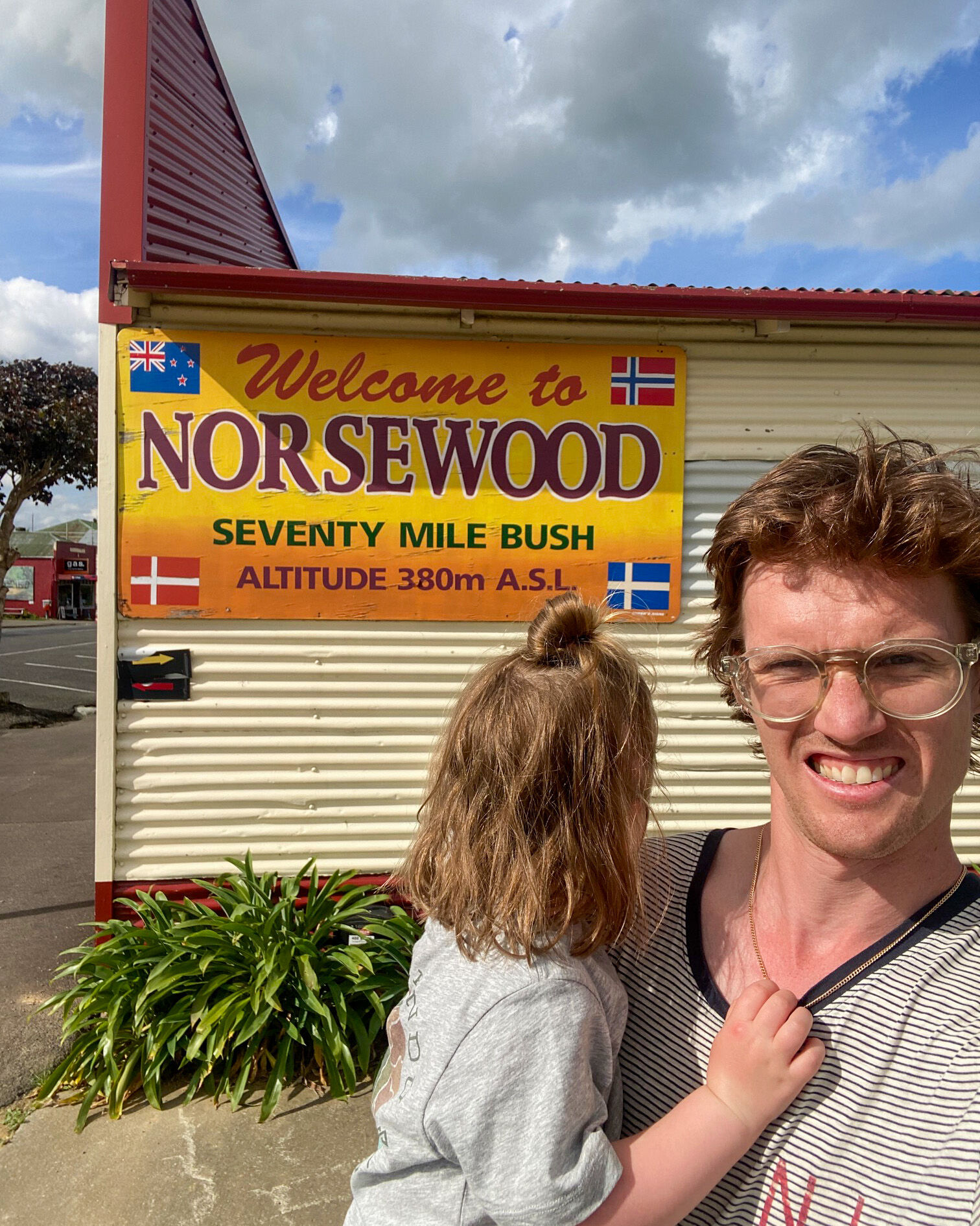 Far med jente på armen foran skilt med Norsevood