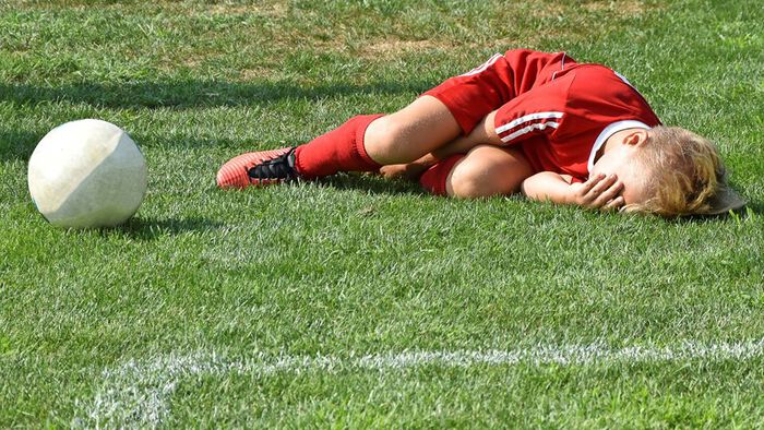 Ung fotballspiller ligger skadet på banen