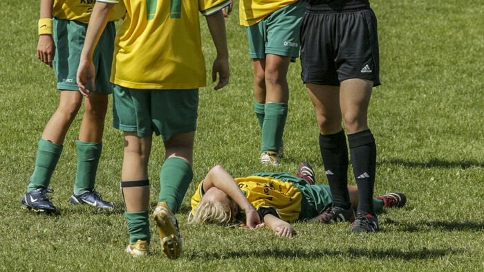 Ung fotballspiller ligger skadet på banen