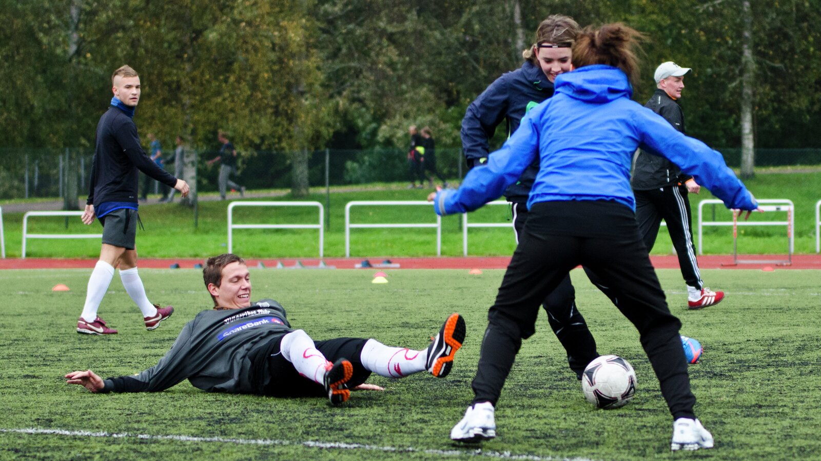 En gutt ligger på bakken etter å ha blitt driblet av to jenter