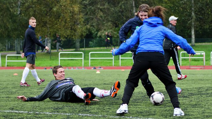 En gutt ligger på bakken etter å ha blitt driblet av to jenter