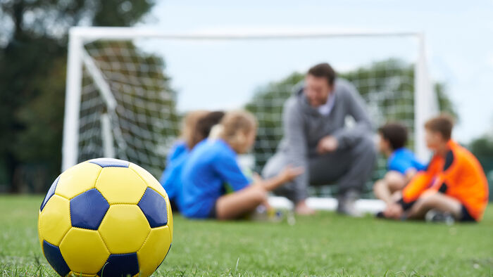 Trener og lag diskuterer taktikk med fotball i forgrunn