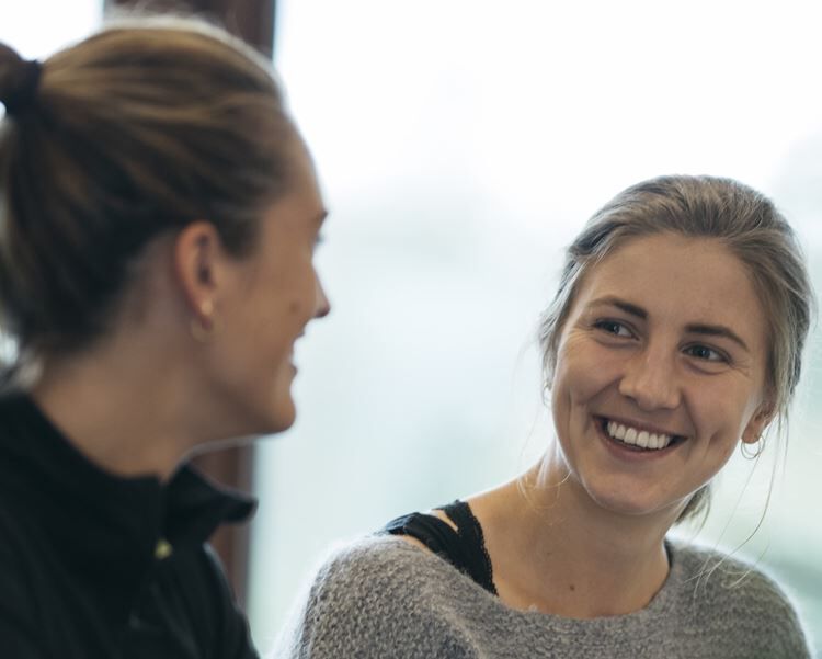 To kvinner smiler til hverandre under en samtale