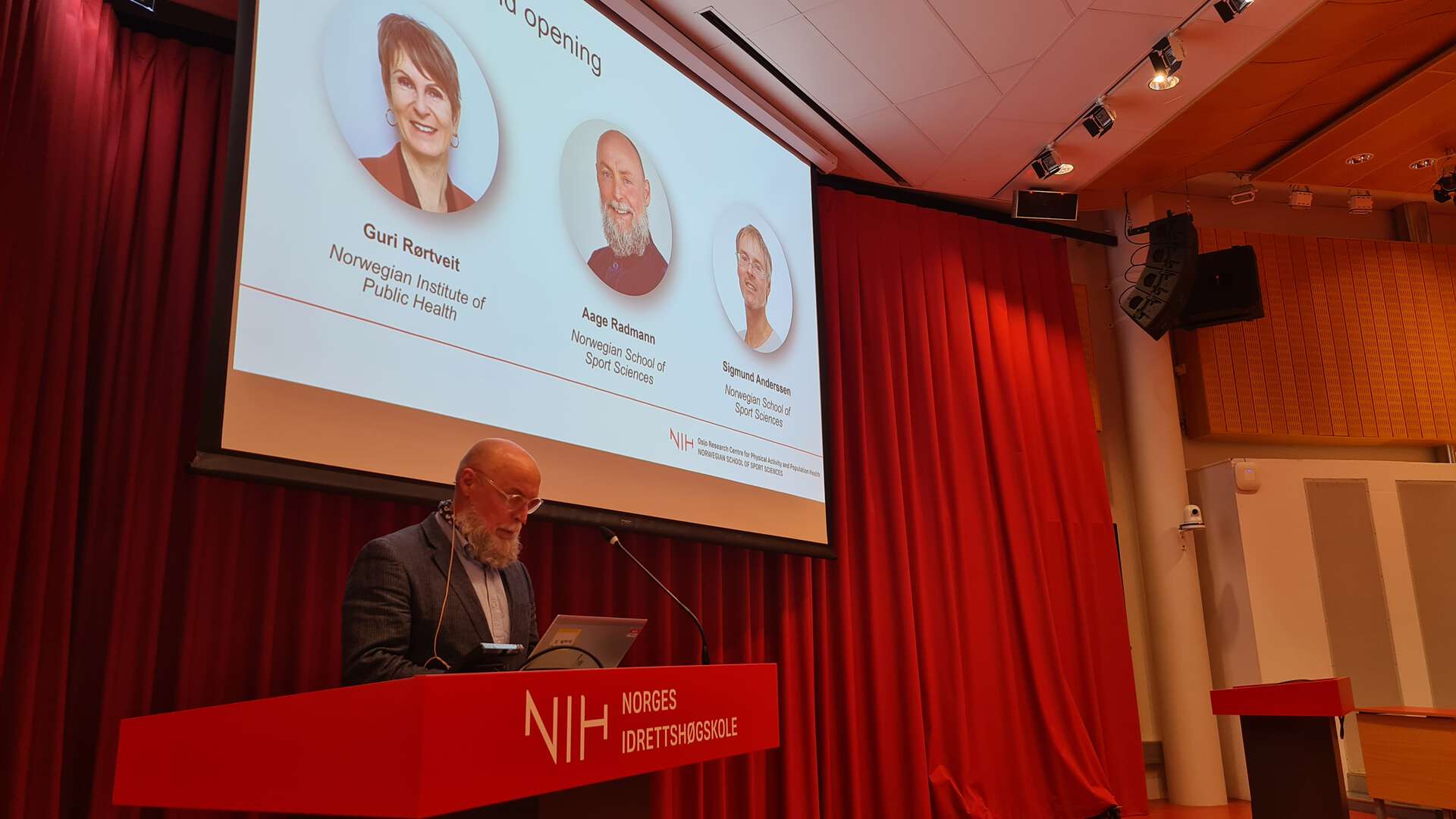 Rektor står foran skjermen og leser fra kortene.