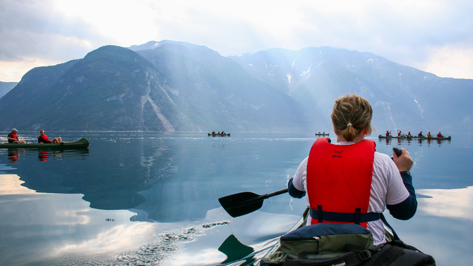 Young woman paddling on still water. Another canoe and mountains in the background