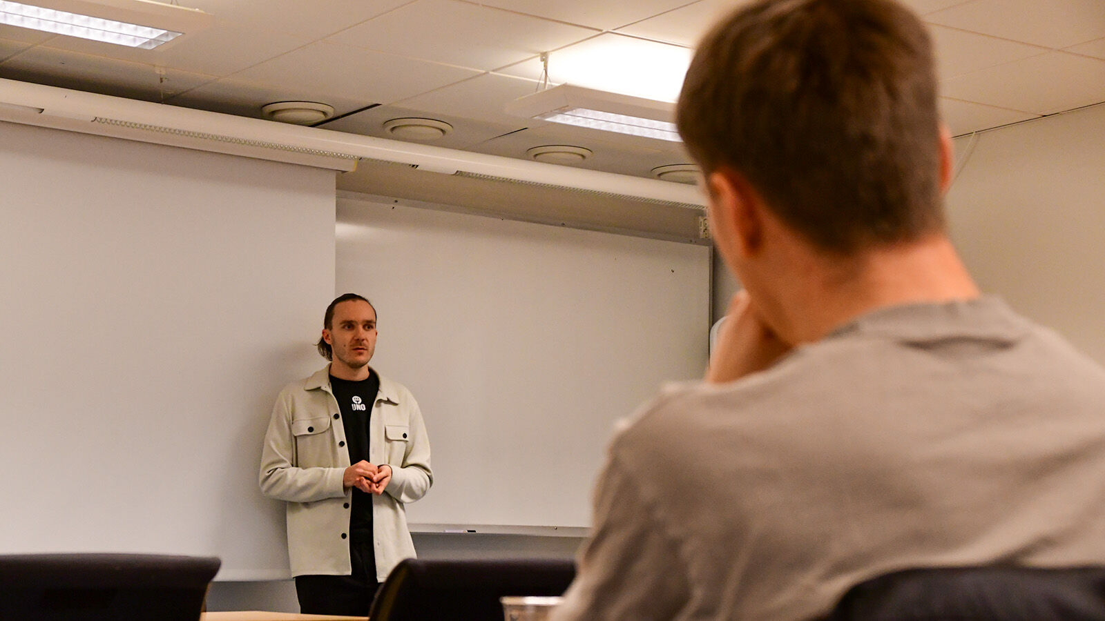 Lærar framme i klasserommet. Student i ufokus