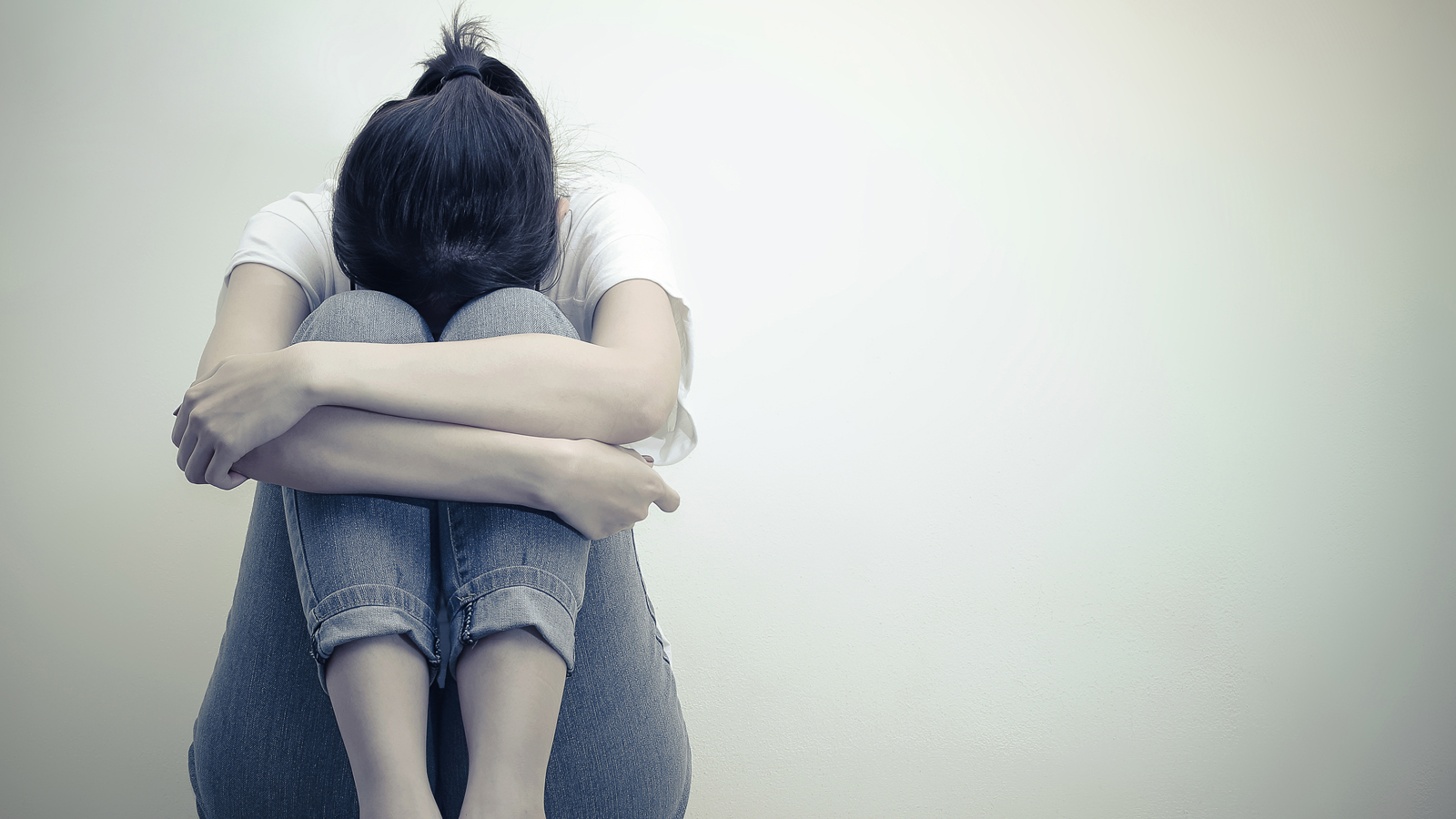 Ung voksen jente sitter med bøyd hode og armene rundt knærne