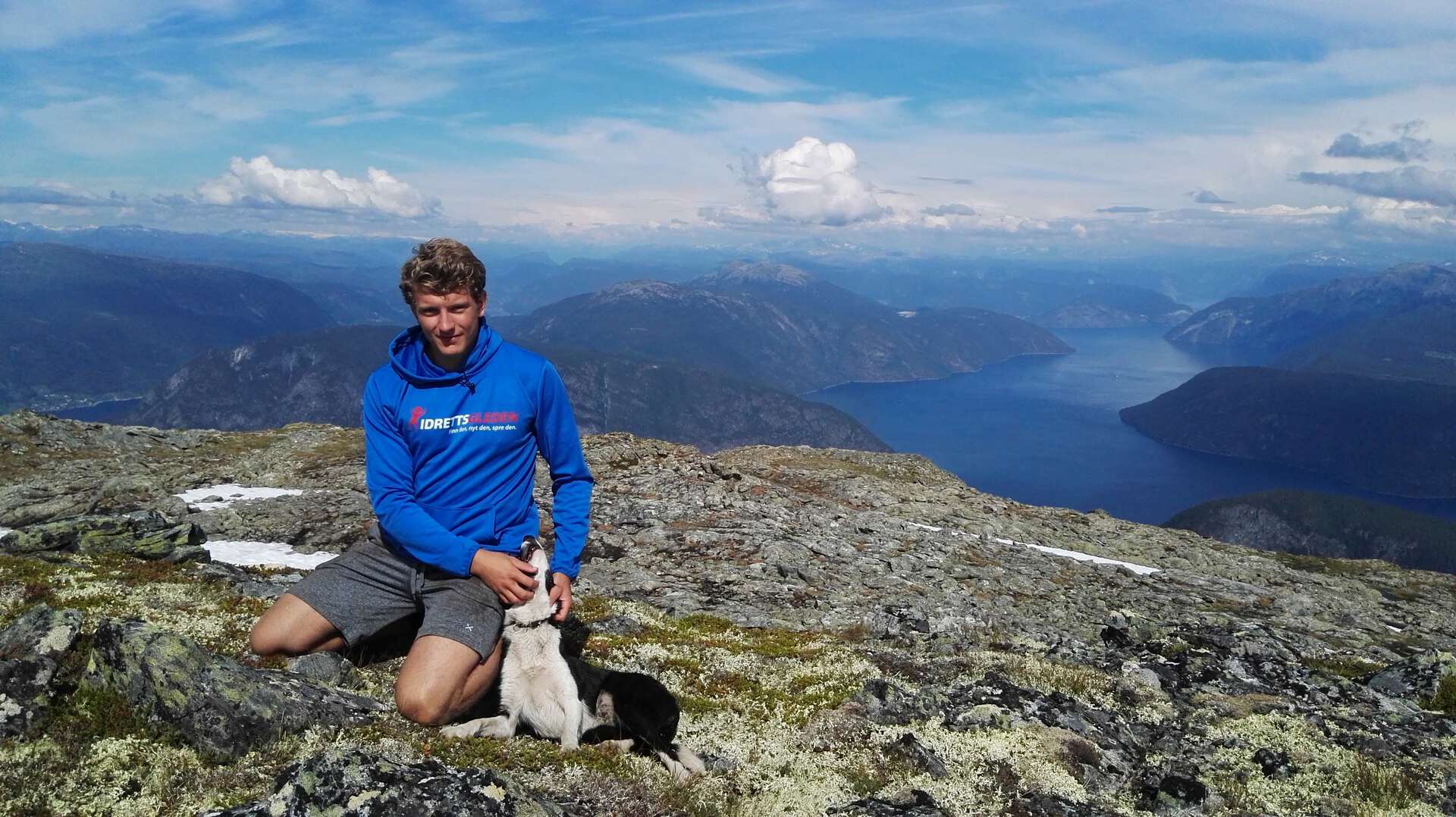 Mann sitter på en fjelltopp med en hund.