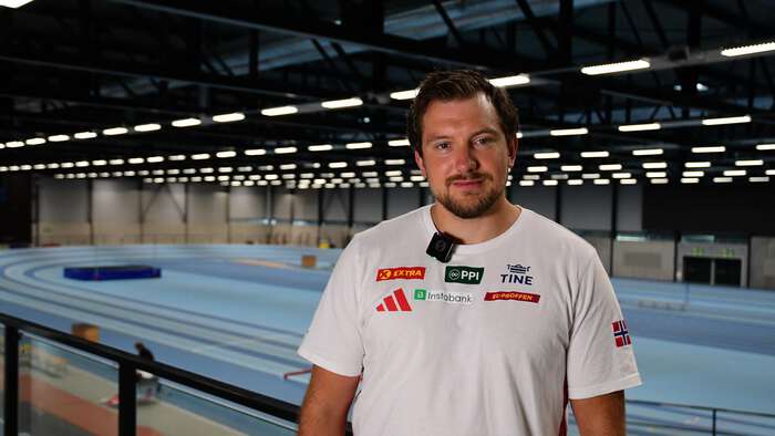 Mann står foran en innendør friidretsbane. 