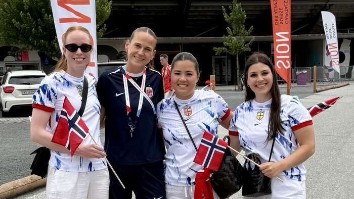 Fire kvinner med fotballtrøyer poserer utenfor fotballstadion. 