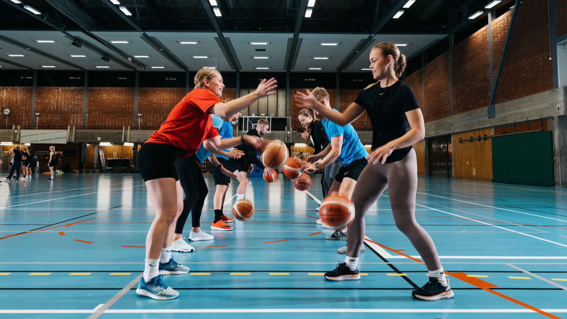 En gruppe studenter står mot hverandre og trikser med basketball.