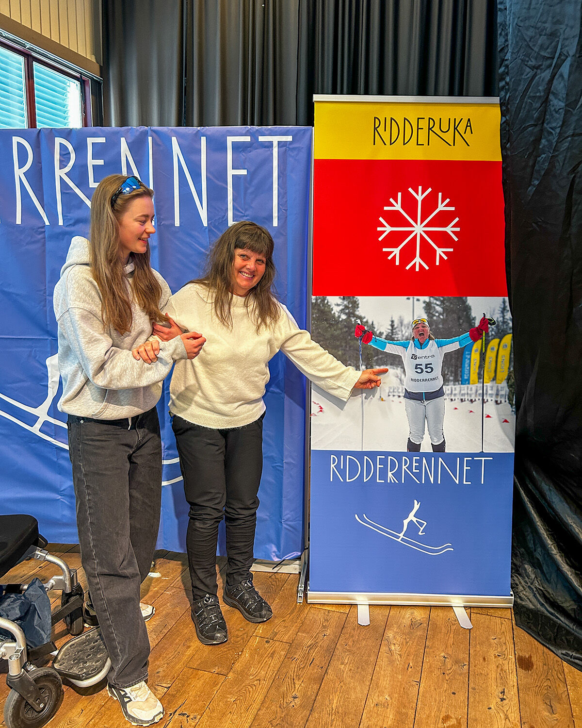 SEva og ledsager foran plakat av Ridderennet